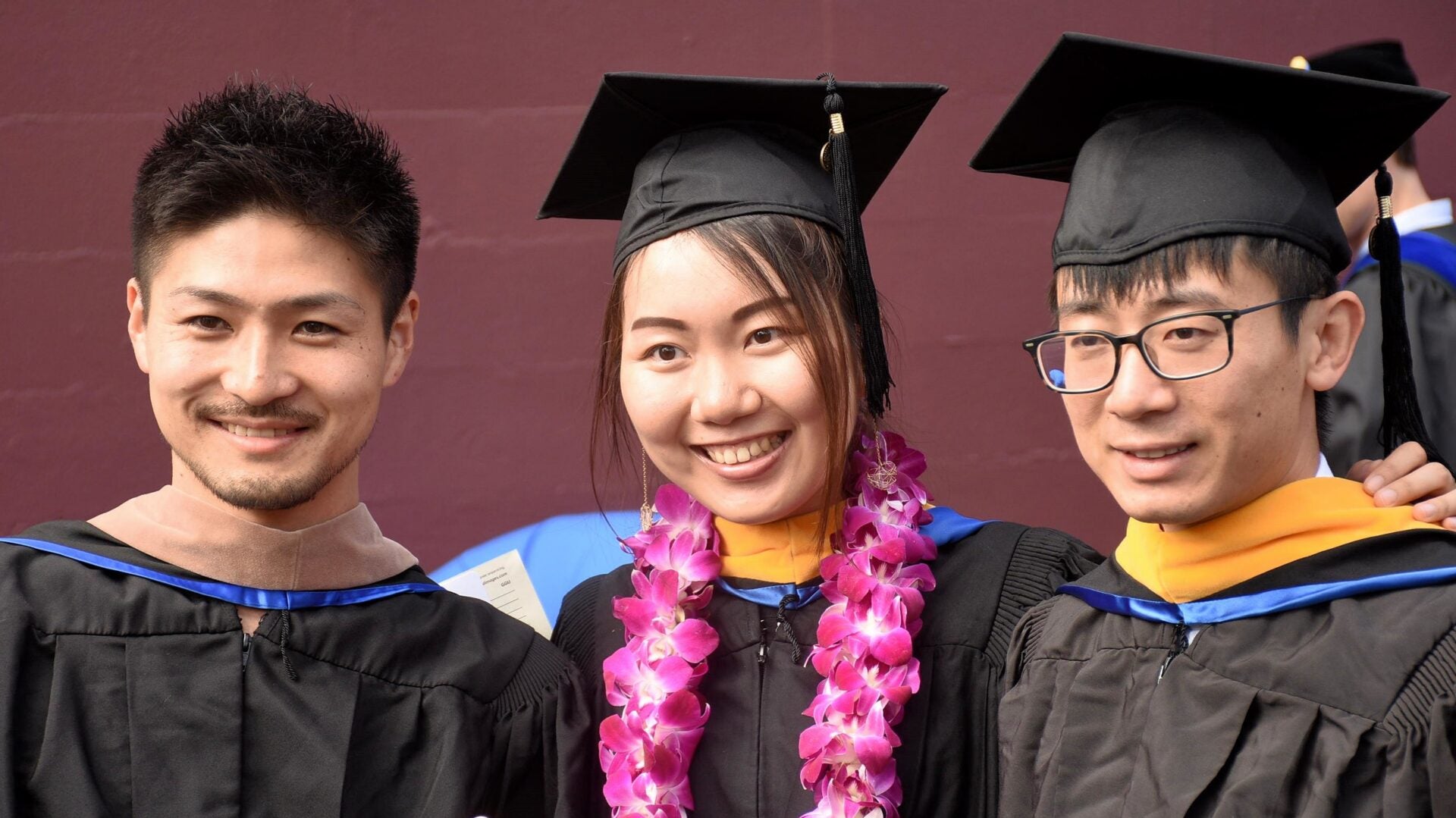 Three graduates wearing academic regalia and smiling.