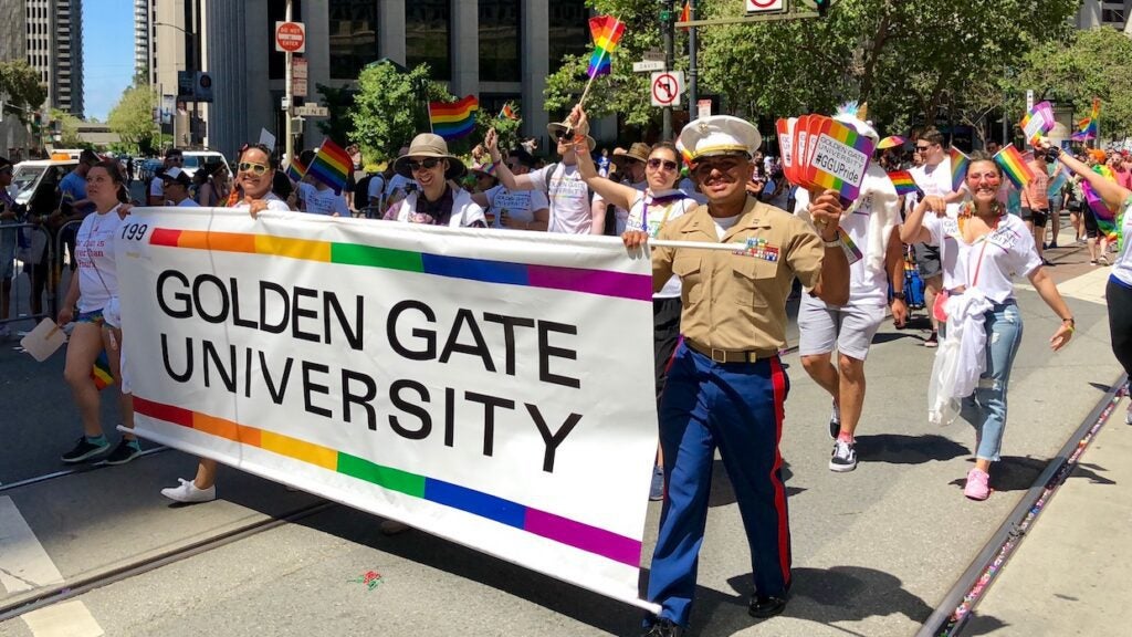 Crowd of people walking with a Golden Gate University banner at a pride parade.
