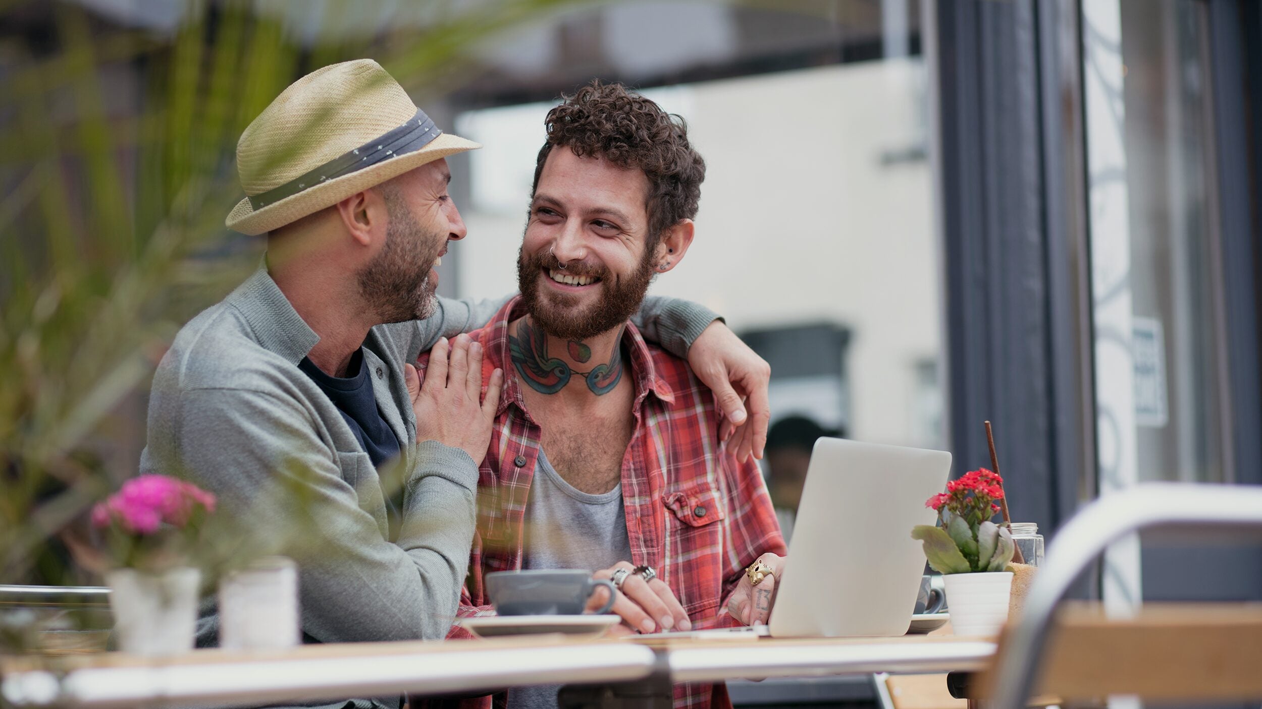 Men smiling outside of cafe on laptop.