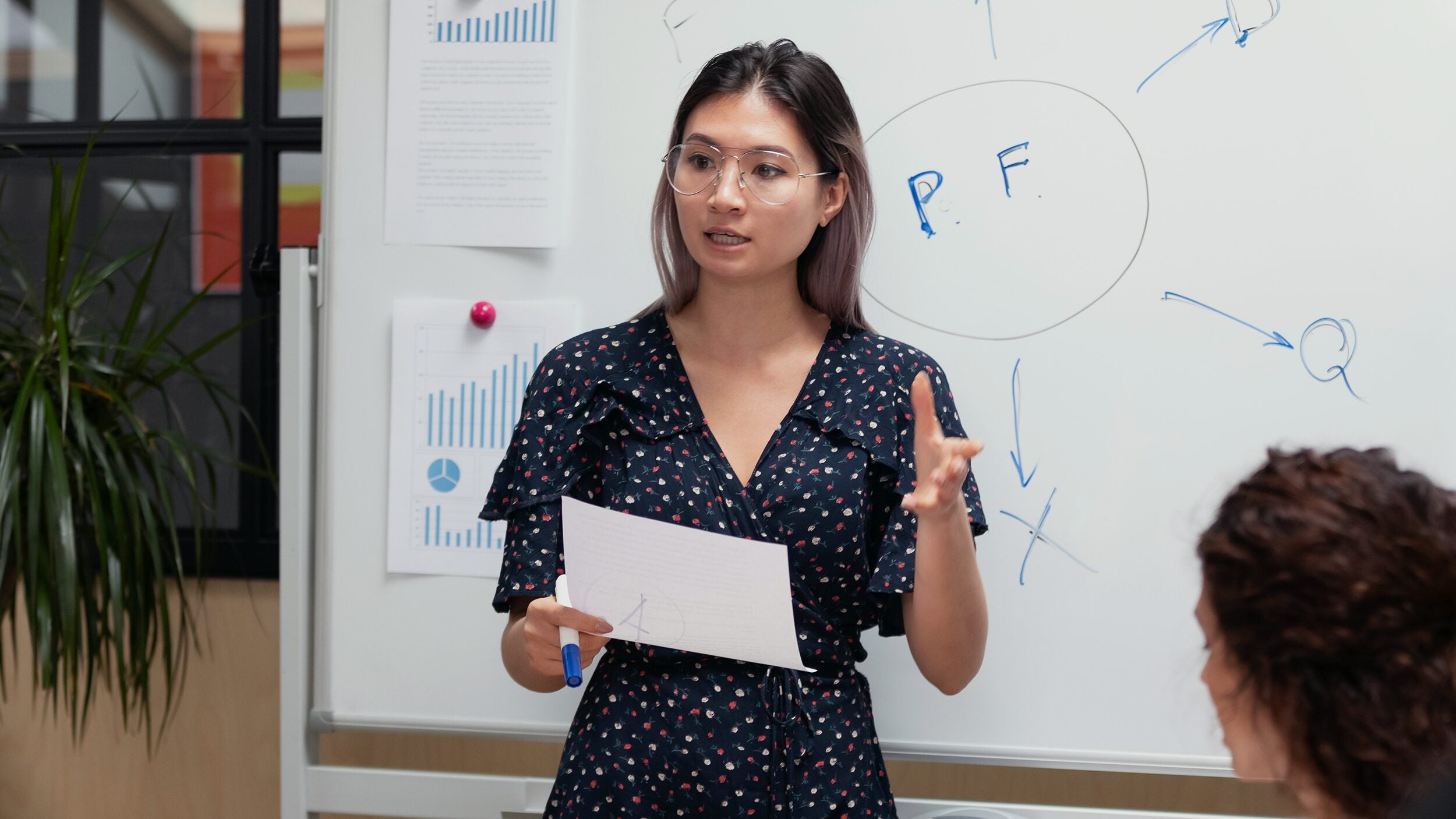 Woman standing in front of a white board, presenting.