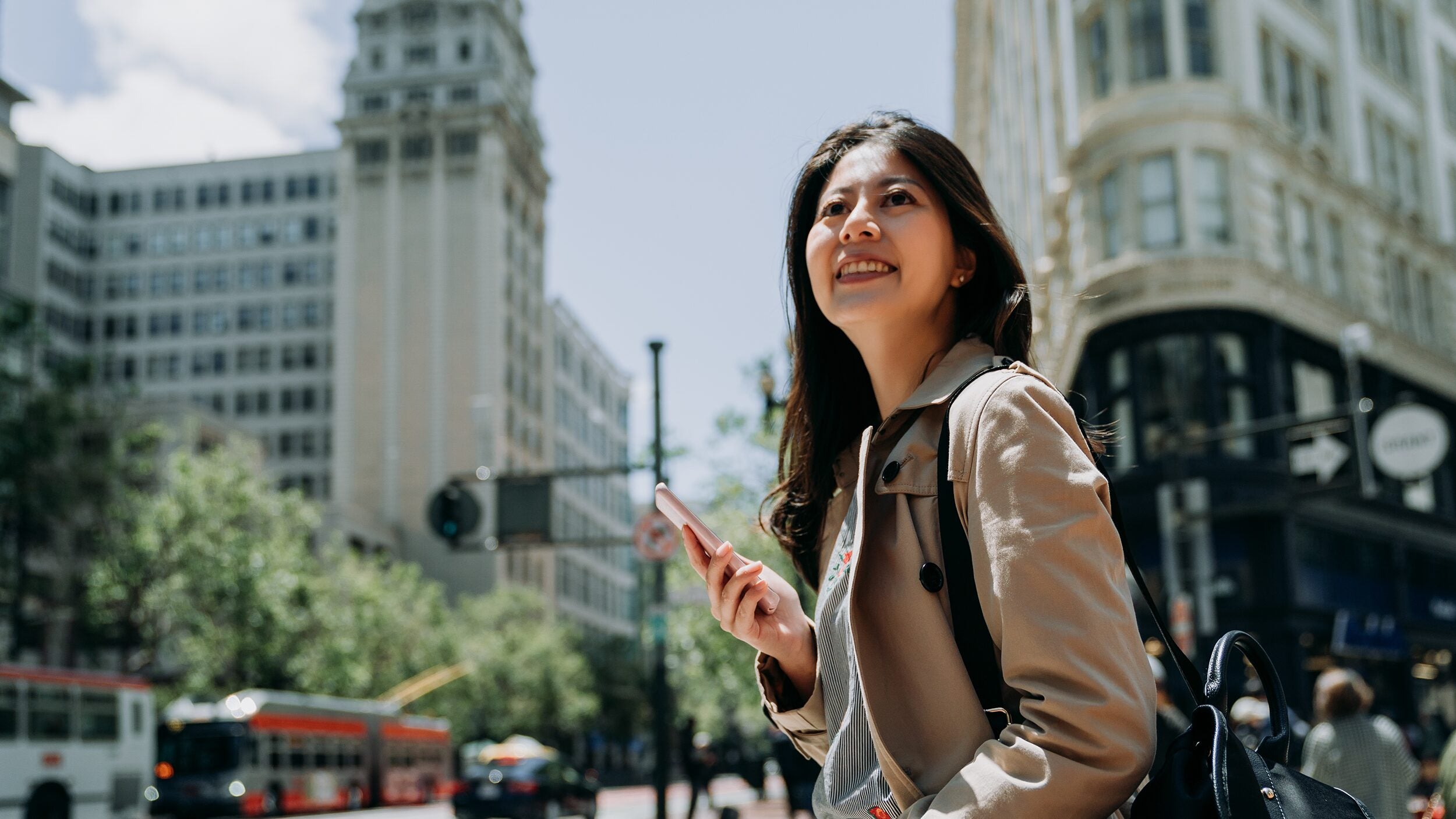 Happy woman holding phone in busy city area in San Francisco.
