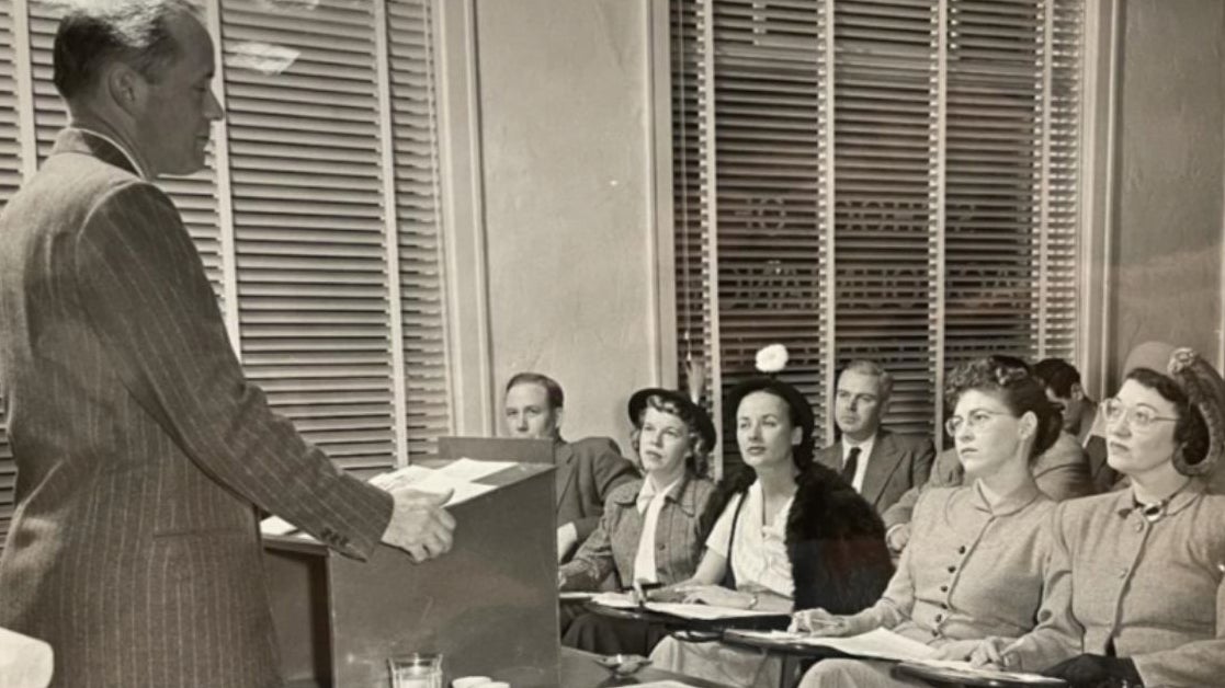 Students in class listening to teacher at podium in 1947.
