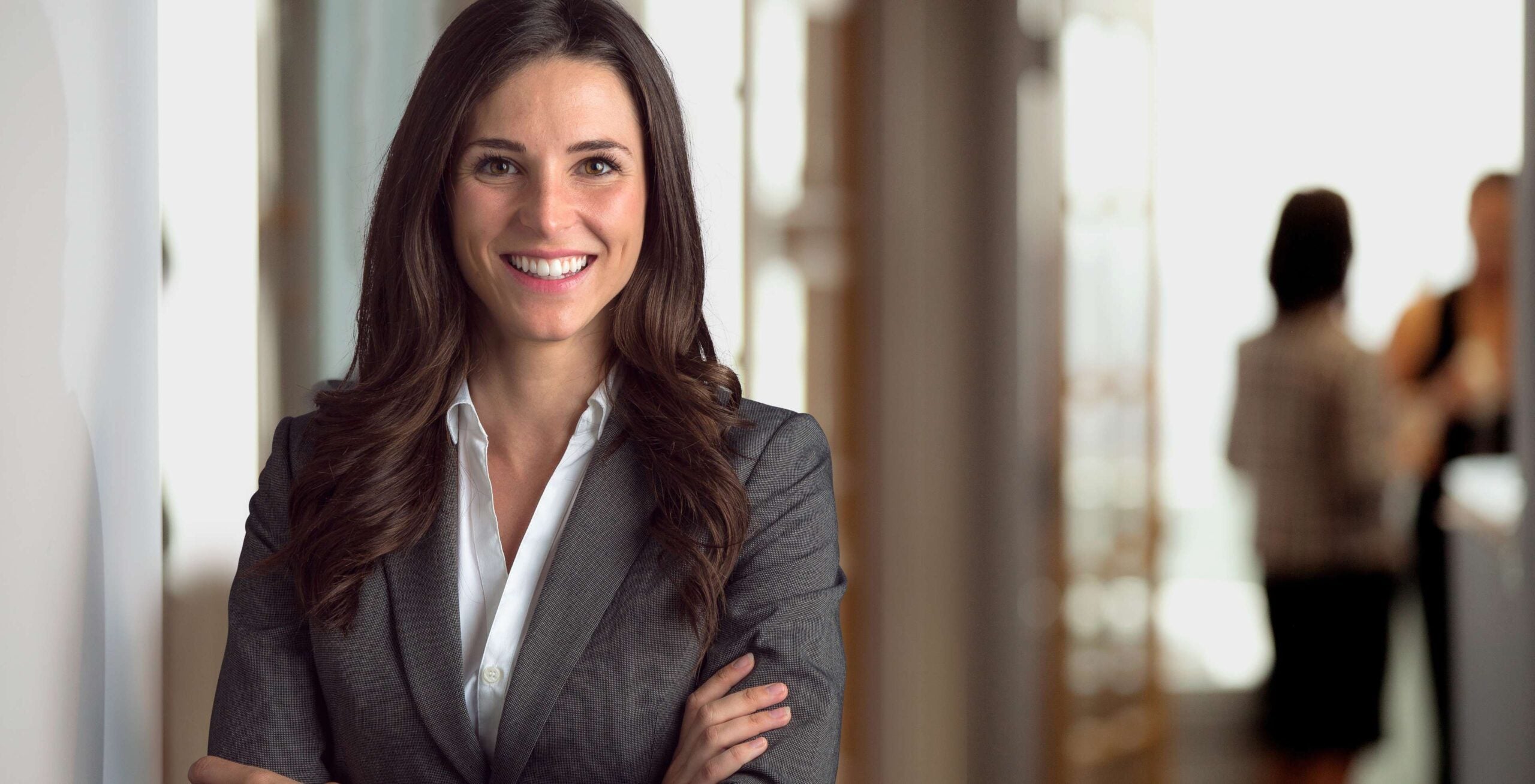 Smiling woman standing in suit with arms crossed.