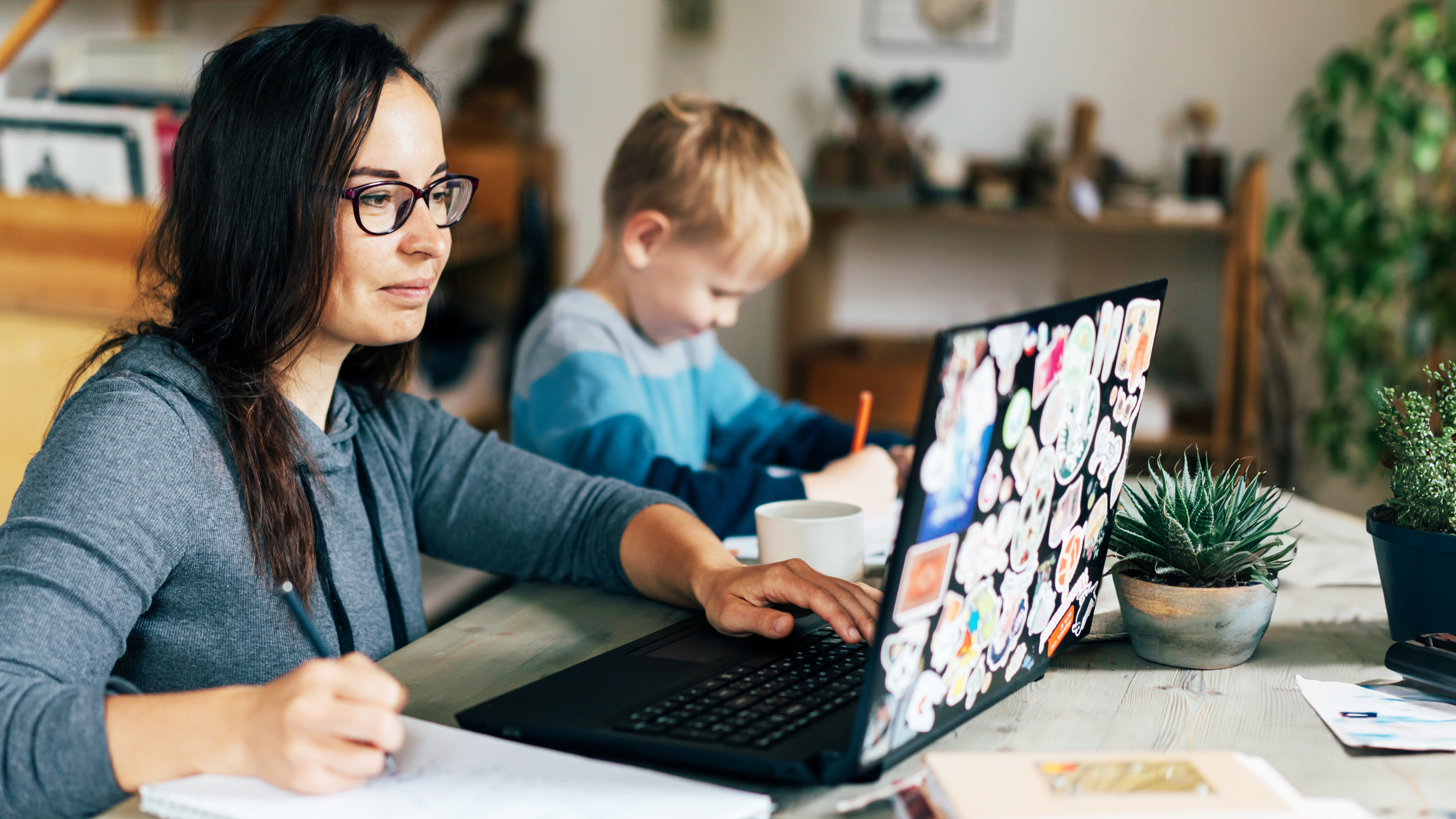 Woman working at kitchen table with child.