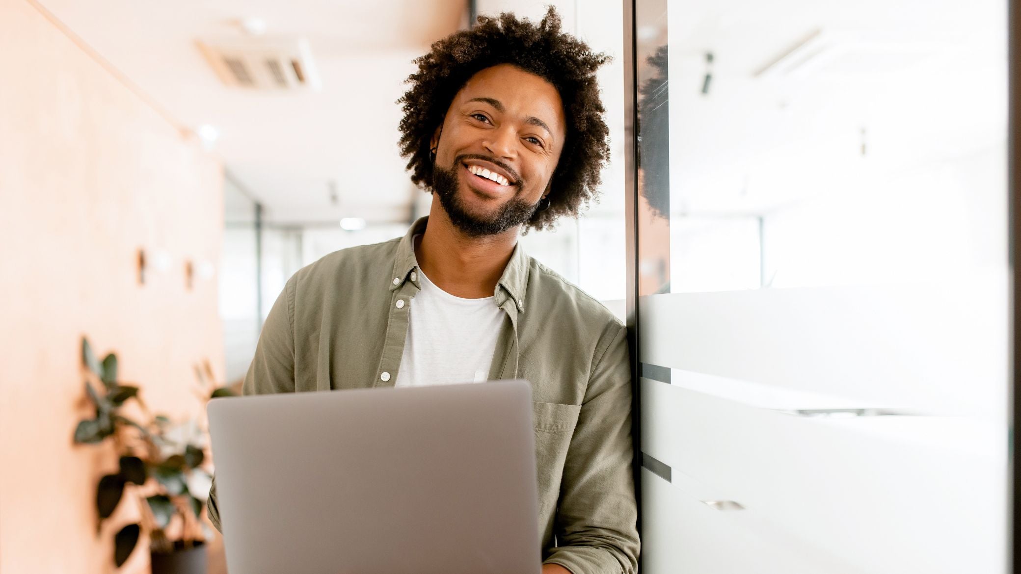 Smiling man standing in an office building with a laptop.