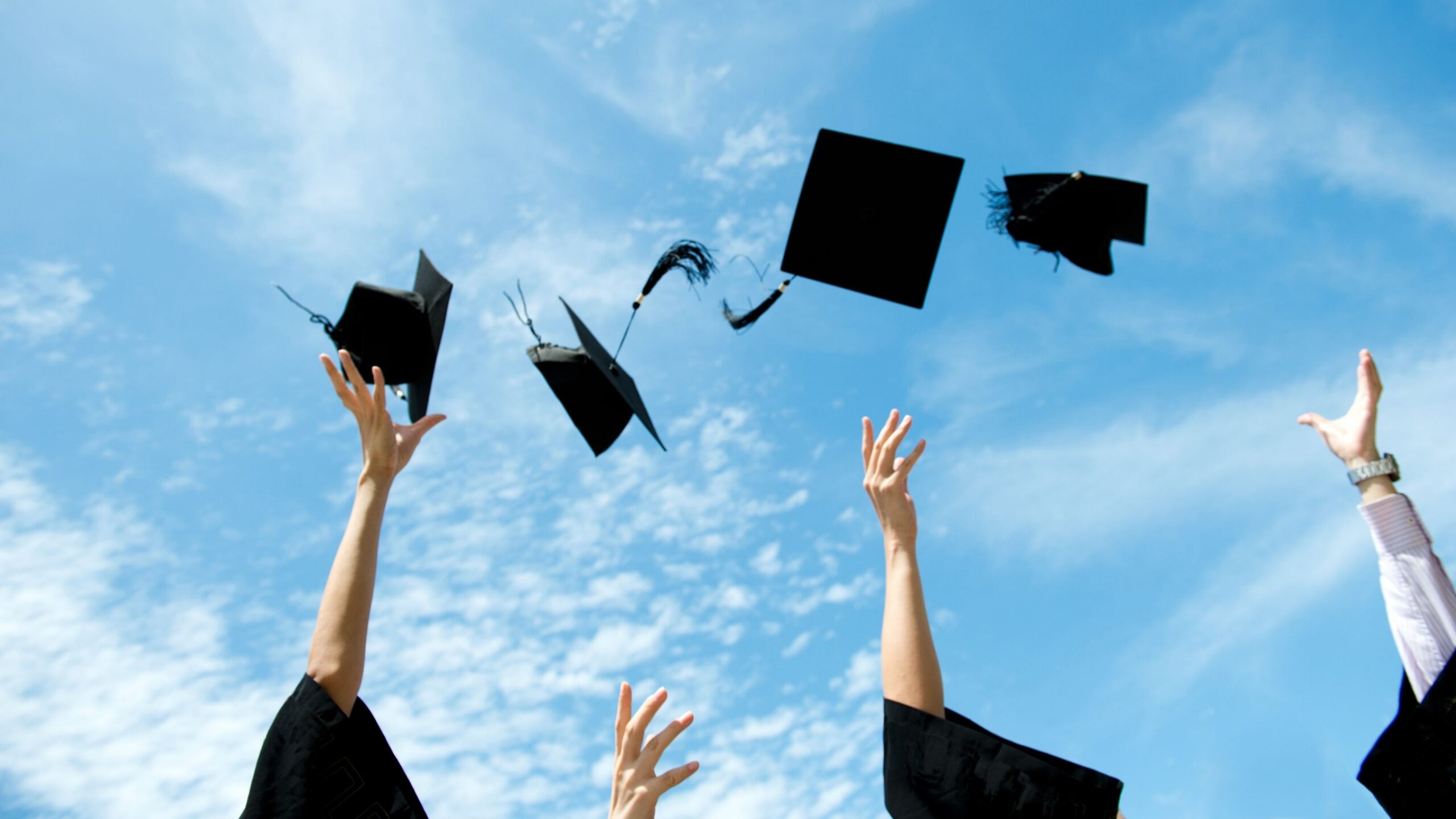 Three to four graduates toss their caps in the air in celebration