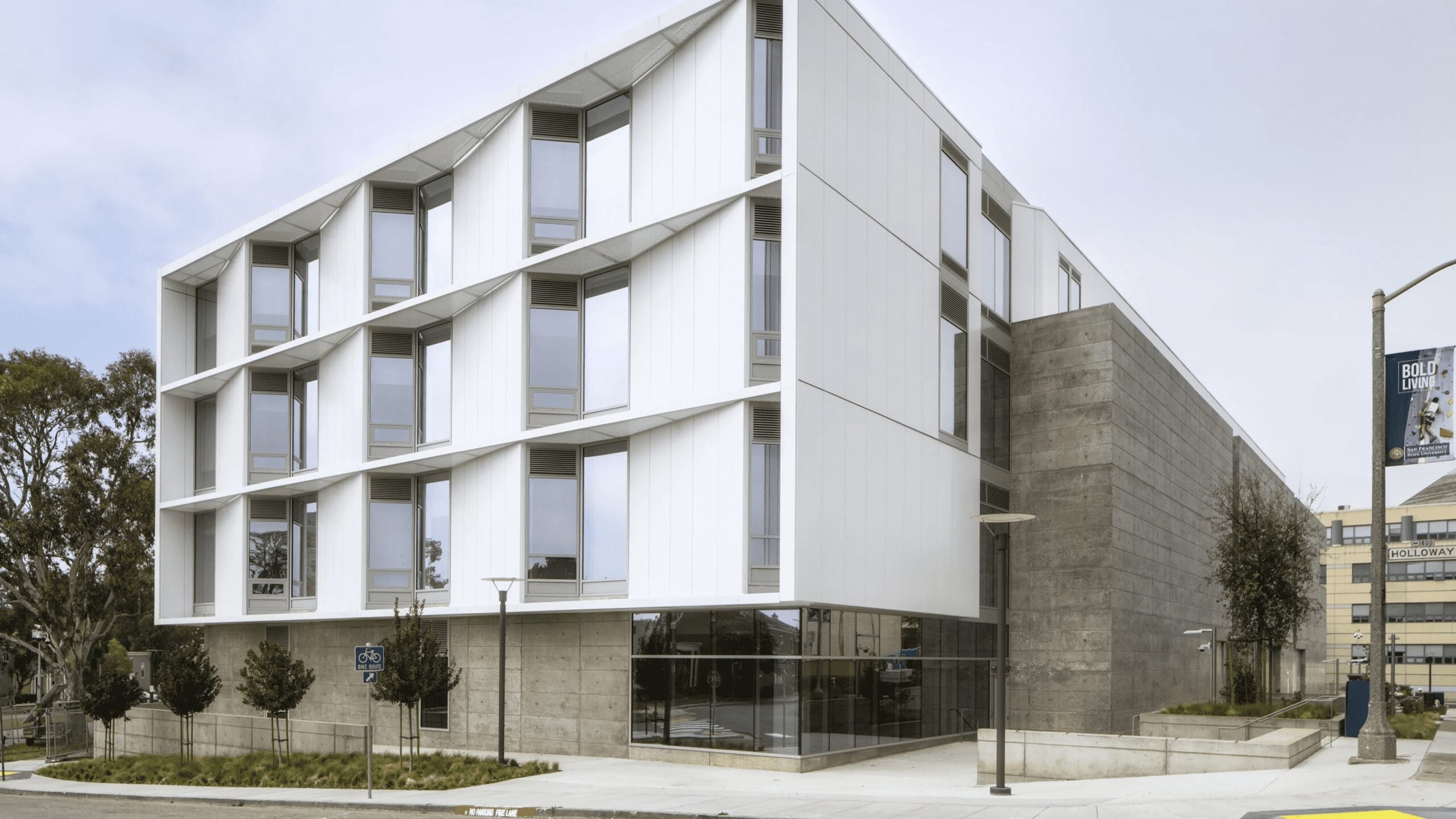 Modern academic building with white architectural panels, expansive windows, and concrete detailing at a street corner.