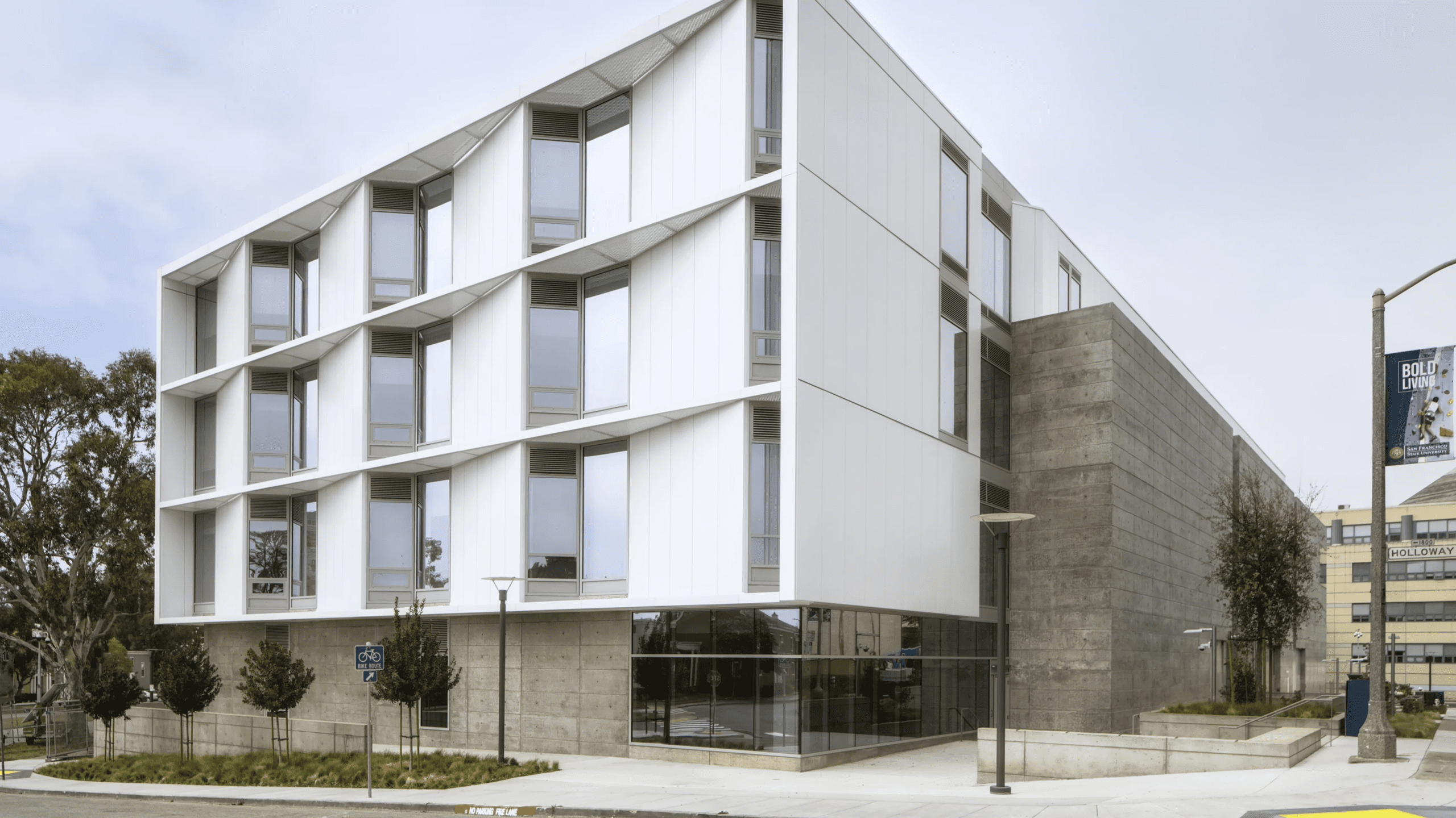 Modern academic building with white architectural panels, expansive windows, and concrete detailing at a street corner.