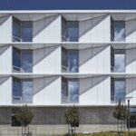Front view of a modern academic building with white exterior panels, large windows, and geometric sun-shading elements.