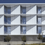 Front view of a modern academic building with white exterior panels, large windows, and geometric sun-shading elements.