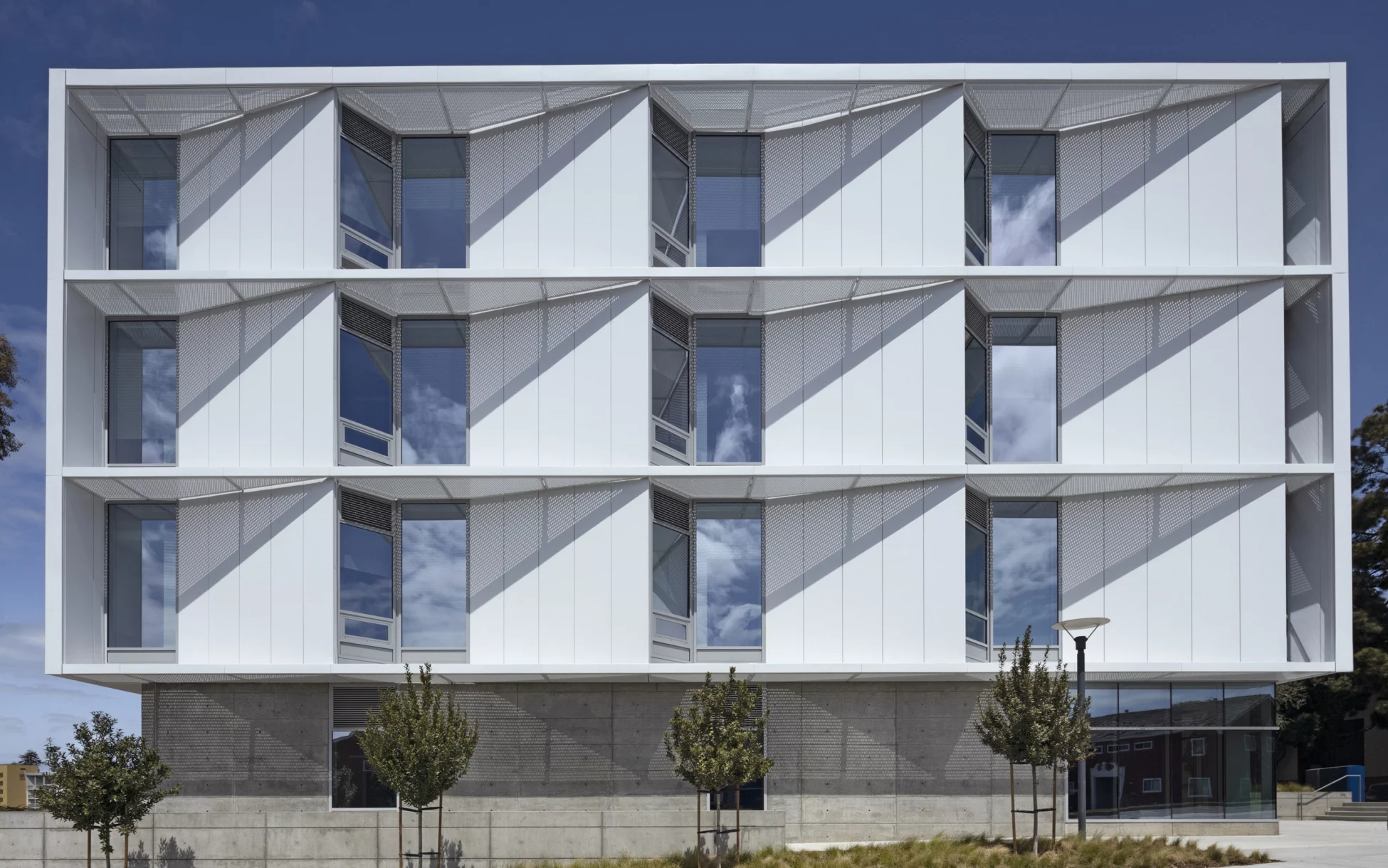 Front view of a modern academic building with white exterior panels, large windows, and geometric sun-shading elements.