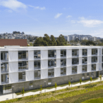 Aerial view of a modern university building surrounded by landscaped grounds and views of the San Francisco skyline.