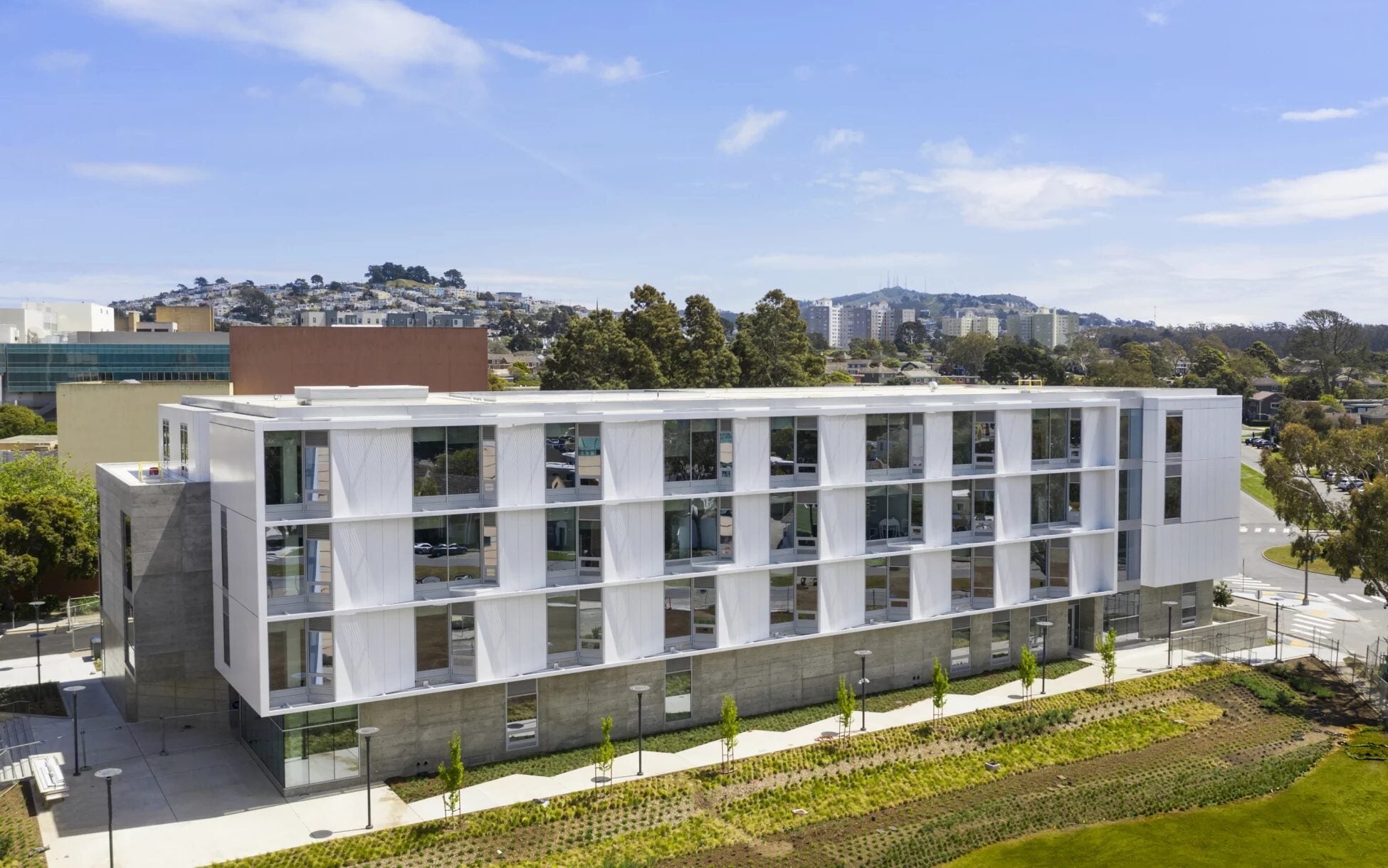 Aerial view of a modern university building surrounded by landscaped grounds and views of the San Francisco skyline.