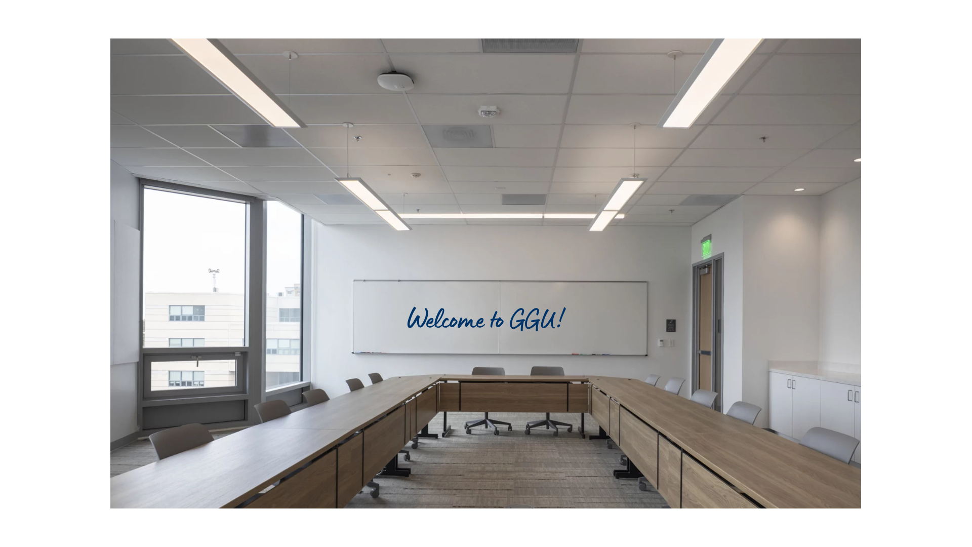 Modern seminar room with U-shaped conference tables and a whiteboard displaying "Welcome to GGU!" in blue handwriting.